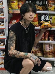 a man with tattoos sitting on the ground in front of a shelf filled with food