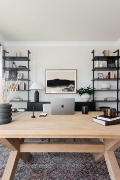 a wooden table with a laptop on it in front of bookshelves and shelves