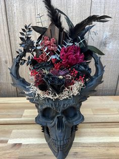 a black skull with flowers and feathers on it's head is sitting on a wooden table