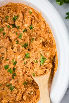 a wooden spoon in a white bowl filled with shredded meat and garnished with cilantro