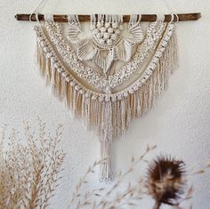 a white wall hanging on the side of a building next to dried grass and plants