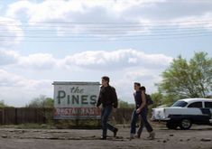 two people walking in front of a sign for the pines restaurant and bar on an old dirt lot