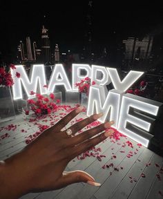 a person's hand reaching for the word marry me in front of rose petals