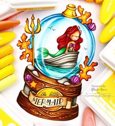 a drawing of a little mermaid in a snow globe surrounded by markers and crayons