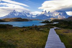 a wooden path leading to a body of water with mountains in the backgroud