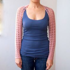 a woman standing in front of a white wall wearing a blue shirt and pink cardigan