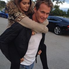 a man carrying a woman on his back while walking down the street with cars behind him