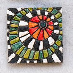 a square shaped tile with multicolored designs on the outside, and an orange circle in the middle