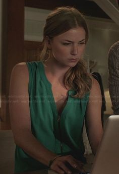 a woman sitting at a table with a laptop computer in front of her and another man standing behind her