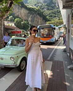 a woman in a white dress eating an ice cream cone on the side of the road