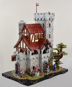 a castle made out of legos on top of a white surface with trees and people