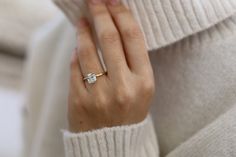 a woman's hand wearing a gold ring with a diamond in the middle and a white sweater