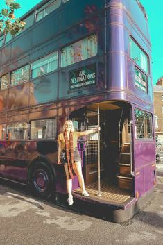 a woman standing in the open door of a double decker bus that is painted purple