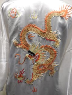 Beautiful Vintage White Chinese Robe/ Dressing gown/ Kimono. 100% Silk and Hand embroidered with a large large Dragon in Bright  Orange, yellow, red and green on the backside and 2 smaller dragons on the frontal area. Because this robe is NWT Deadstock. I have not removed the belt from the original way it came, therefor my pictures are with it just simply open. This is such a nice airy  and flowy dressing gown in a Bright White, which is fairly hard to find. Makes for an excellent gift. Tagged a Chinese Embroidery Design, Chinese Dressing, Chinese Kimono, Chinese Embroidered, Chinese Embroidery, Womens Robes, Bright Orange, Bright White, White Vintage