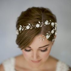 a woman wearing a bridal headpiece with flowers and pearls on her hair is looking down