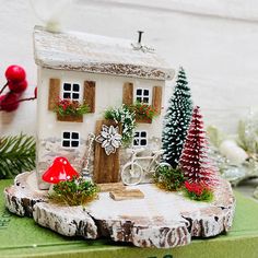 a christmas scene with a small house on a tree stump and decorations around the base