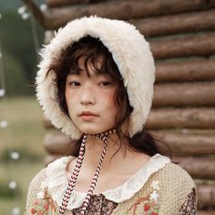 a young woman wearing a hat and holding a string in front of her head with logs behind her