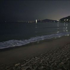 the beach at night with waves coming in from the water and buildings on the horizon