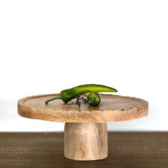 two green peppers sitting on top of a wooden plate