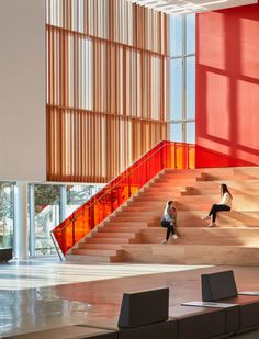 two people are sitting on the stairs in front of a red wall and large windows