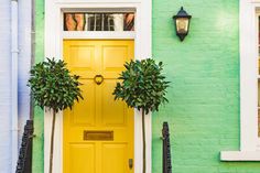 two potted plants are on the front door of a green brick house with white trim