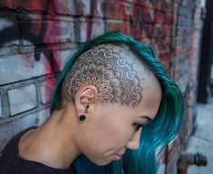 a woman with green hair has a tattoo on her head and is looking down at the ground