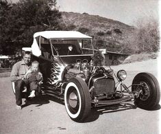 an old black and white photo of a man holding a child in front of a car