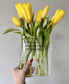 a hand holding a clear vase with yellow flowers in it and the words tulips, beatifully enamoment