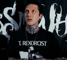 a man with tattoos and piercings standing in front of a black background wearing a t - shirt