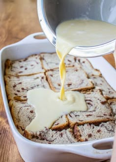 someone pouring sauce on some bread in a white casserole dish with other food items