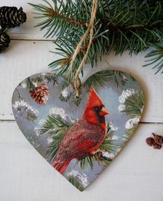 a heart shaped ornament with a cardinal on it hanging from a pine tree