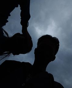 the silhouette of two people against a cloudy sky