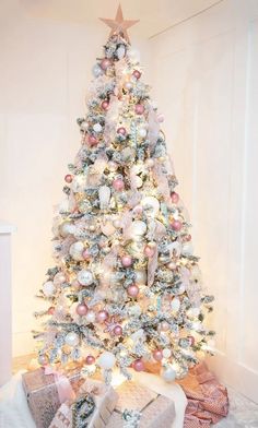 a white christmas tree with pink and silver ornaments on it's branches, surrounded by presents