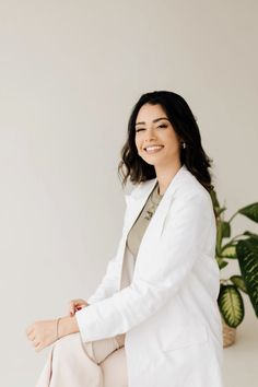 a woman sitting on top of a white chair next to a potted green plant