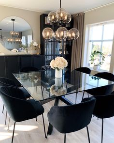 a dining room table with black chairs and a clear glass top centerpiece in front of a large window