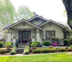 a house that is in the middle of some grass and trees with bushes around it