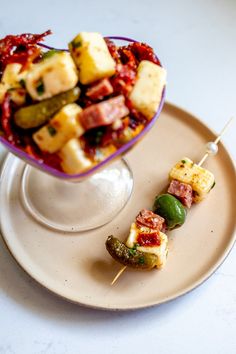 a plate with skewered food on it next to a bowl filled with vegetables