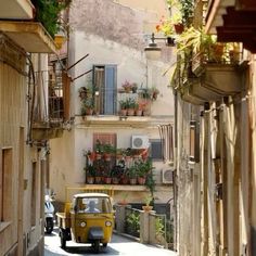 an old yellow car driving down a narrow street