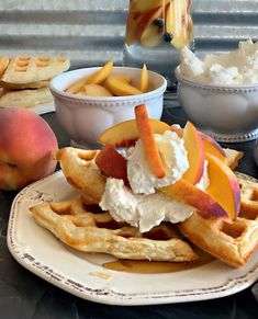 a plate with waffles, peaches and ice cream on it next to bowls of fruit