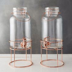 two glass jars sitting on top of metal stand next to each other, one with a copper handle