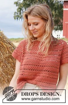 a woman standing in front of hay bales wearing an orange crochet top