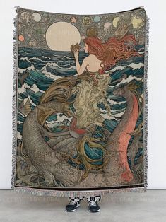 a tapestry with a mermaid sitting on it's back in front of the ocean