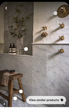 a bathroom with white marble walls and flooring next to a wooden stool in front of a window