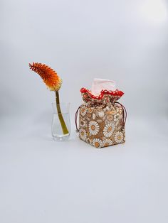 a small purse sitting next to a vase with a flower in it on a white surface