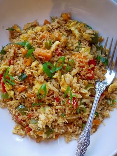 a white plate topped with fried rice and veggies next to a silver fork