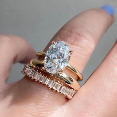 a woman's hand with three different rings on top of her finger and the ring has an oval shaped diamond surrounded by baguets