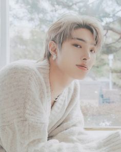 a man sitting on top of a window sill next to a white blanket and a tree