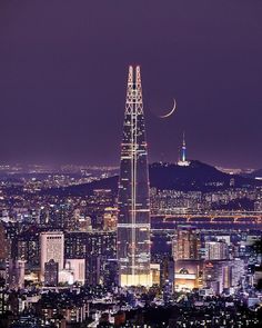 the moon is setting over the city lights and skyscrapers in this nighttime view from atop a hill