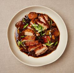 a white plate topped with meat covered in gravy and garnished with green onions