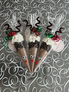 three cones decorated with reindeer noses and candy canes on top of a patterned tablecloth